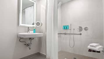 A modern bathroom with a sink, mirror, shower, and towel rack.