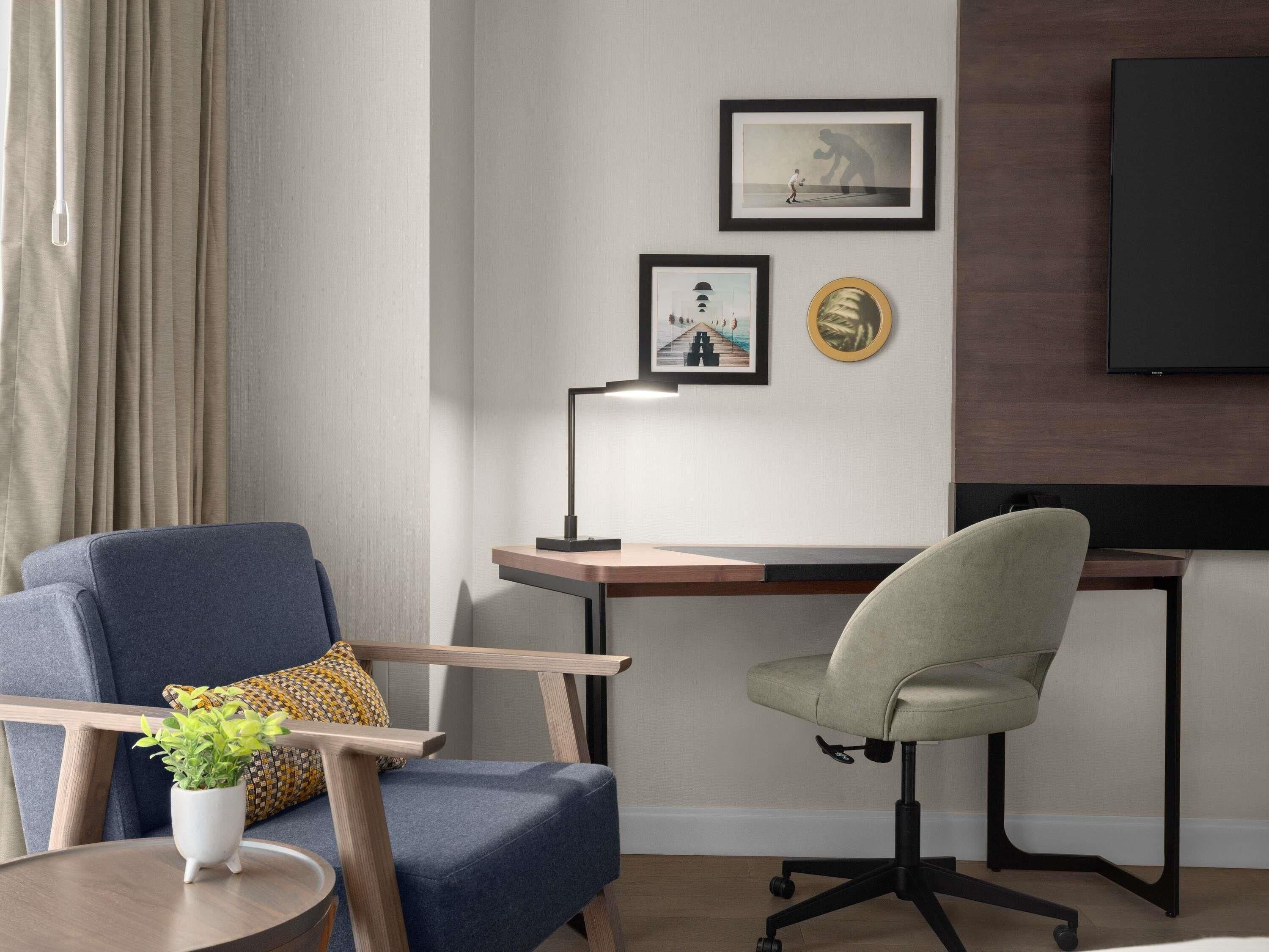 Una habitación moderna con escritorio, dos sillas, lámpara, televisión y cuadros en la pared.