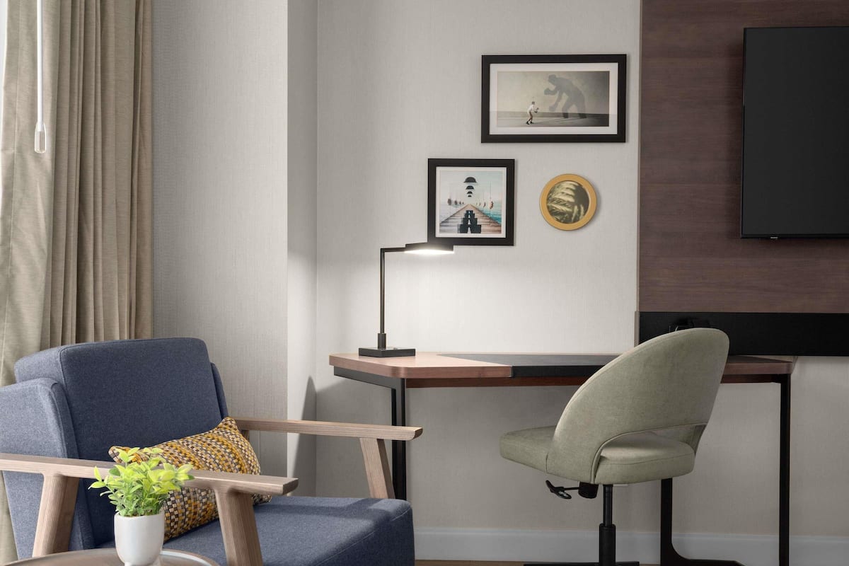 Una habitación moderna con escritorio, dos sillas, lámpara, televisión y cuadros en la pared.
