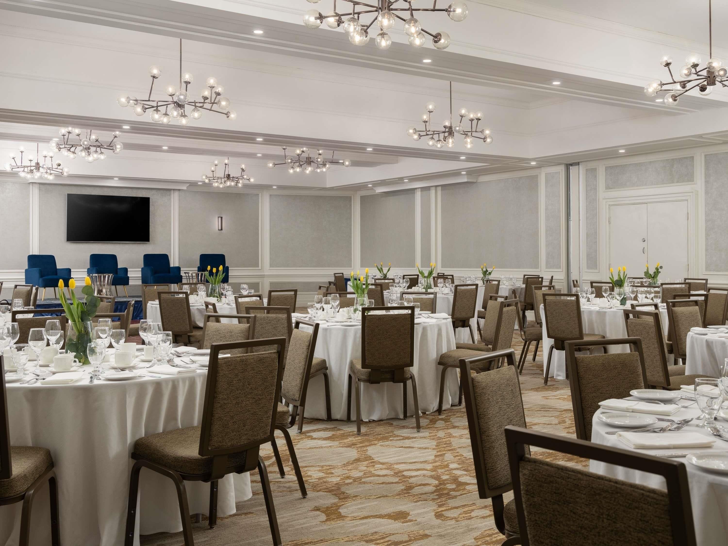 A banquet hall with round tables, chairs, and chandeliers.