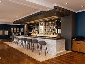 A bar area with a marble countertop, bar stools, and a variety of bottles.