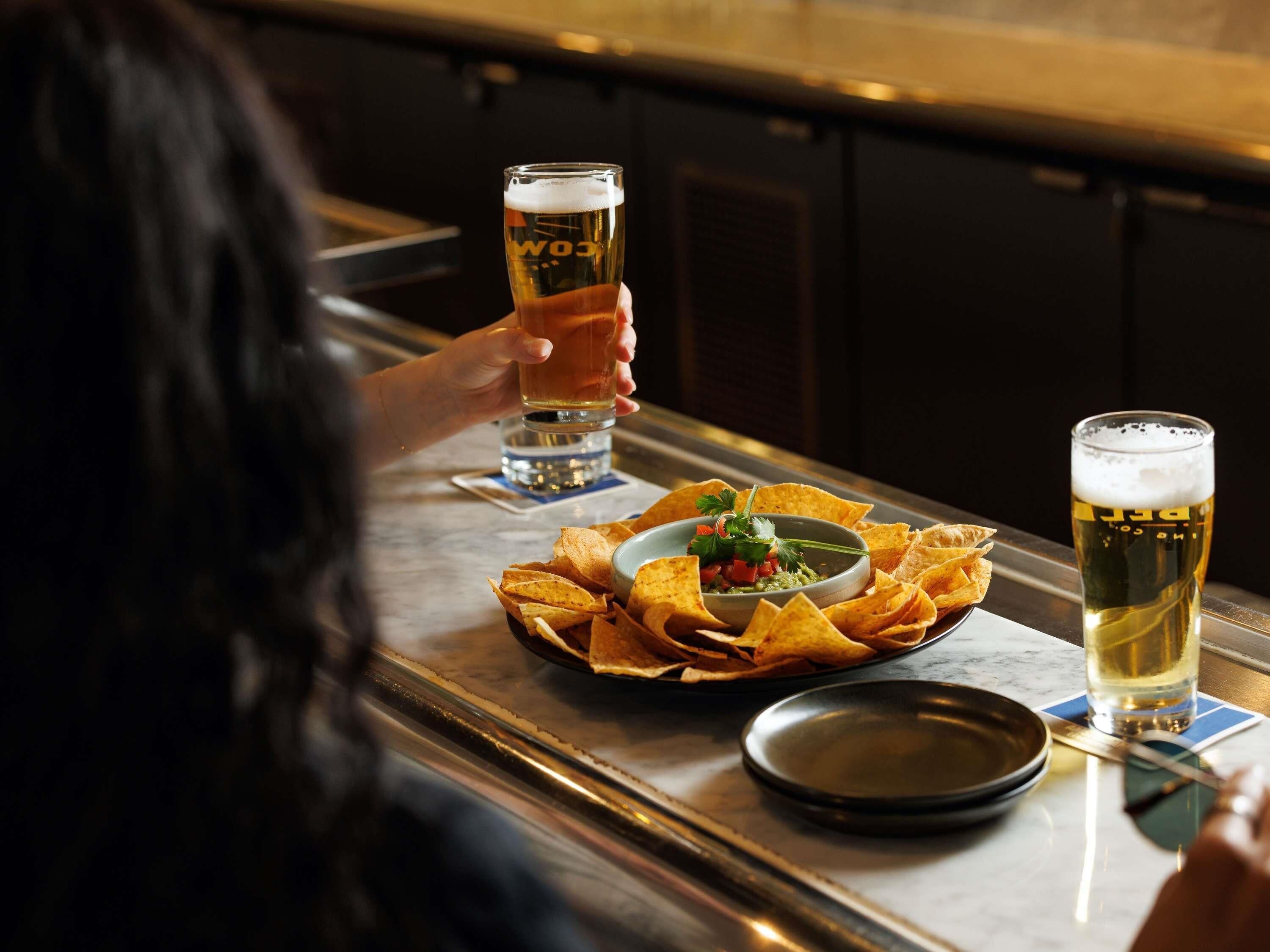 Un bar avec deux verres de bière, un bol de chips et une petite assiette de salsa.