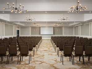 Un salón de conferencias con filas de sillas, piso alfombrado y candelabros.