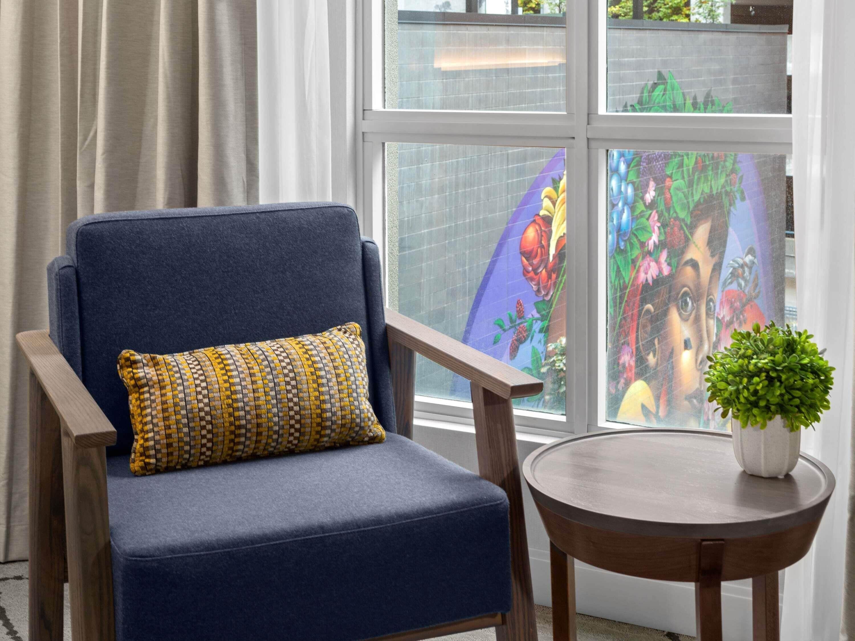 Un sillón azul con un cojín estampado, una mesita redonda de madera y una planta en maceta.