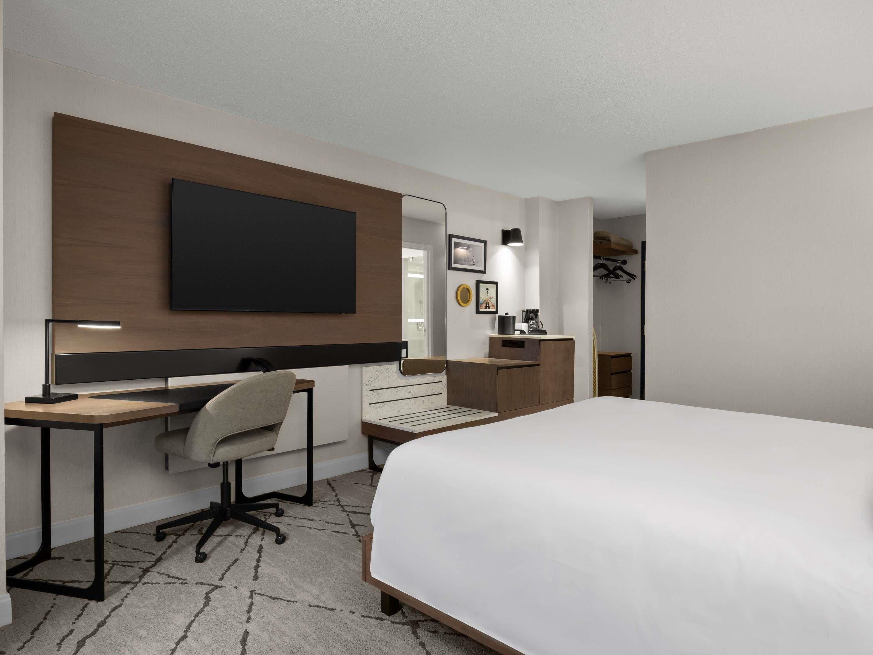 A hotel room with a bed, desk, chair, and a TV mounted on the wall.