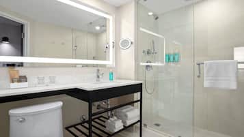 A modern bathroom with a glass-enclosed shower, a large mirror, a white toilet, and a black towel rack.