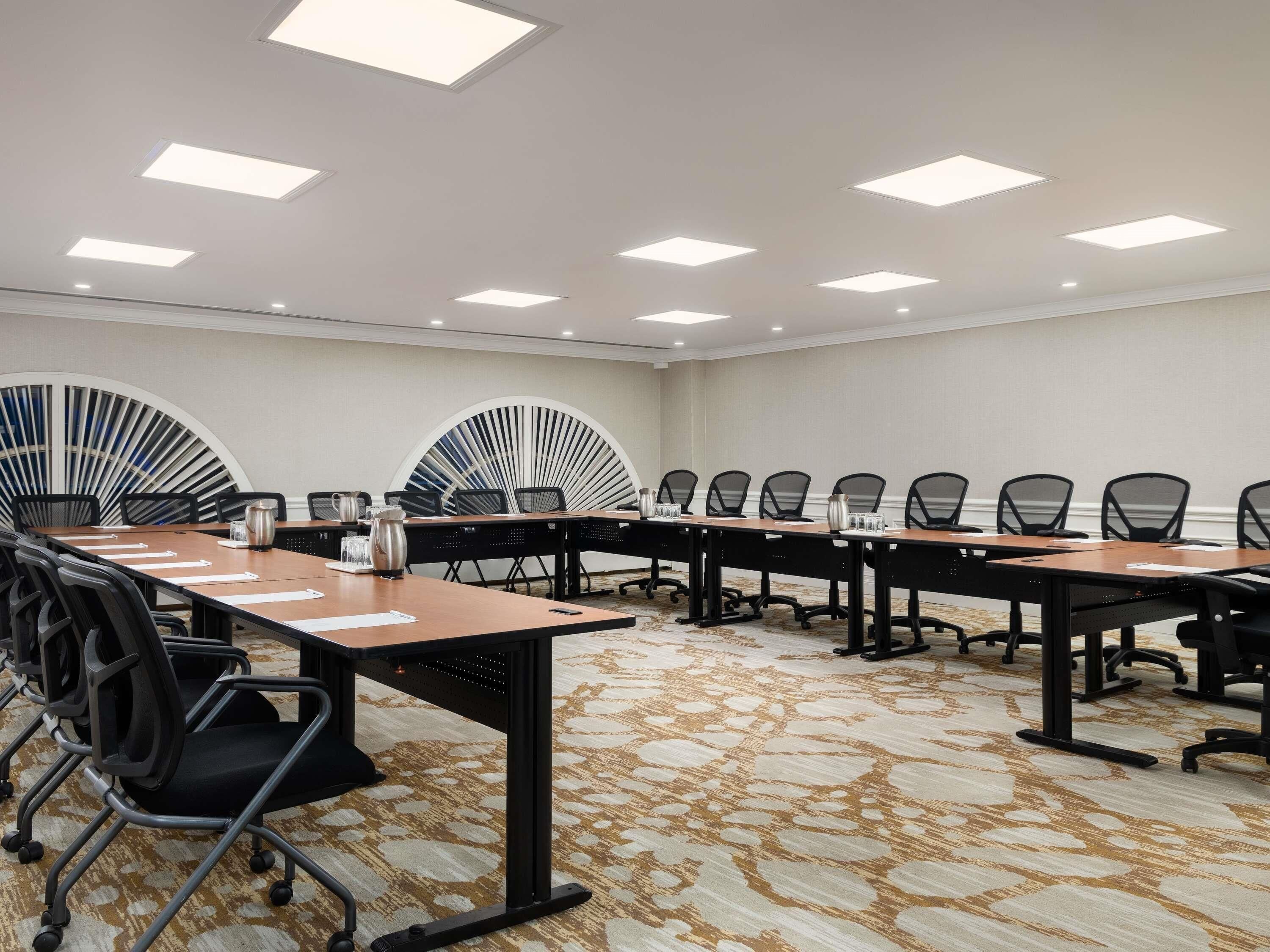A conference room with long tables, chairs, and a patterned carpet.
