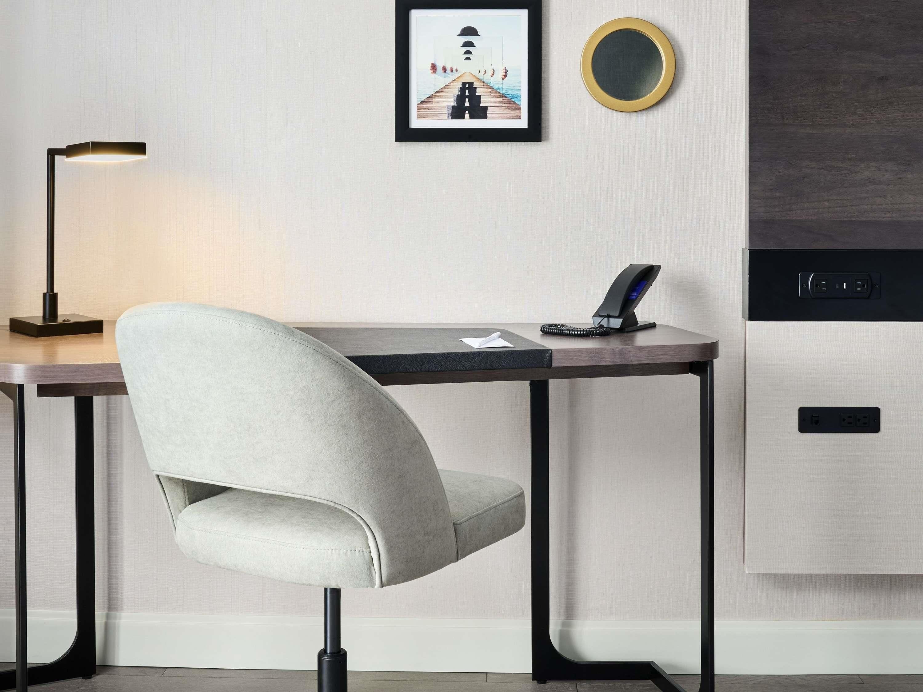 Een moderne bureaustoel, een bureau met een laptop, een lijst met afbeelding, een ronde spiegel en een inbouwapparaat.