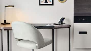 Een moderne bureaustoel, een bureau met een laptop, een lijst met afbeelding, een ronde spiegel en een inbouwapparaat.