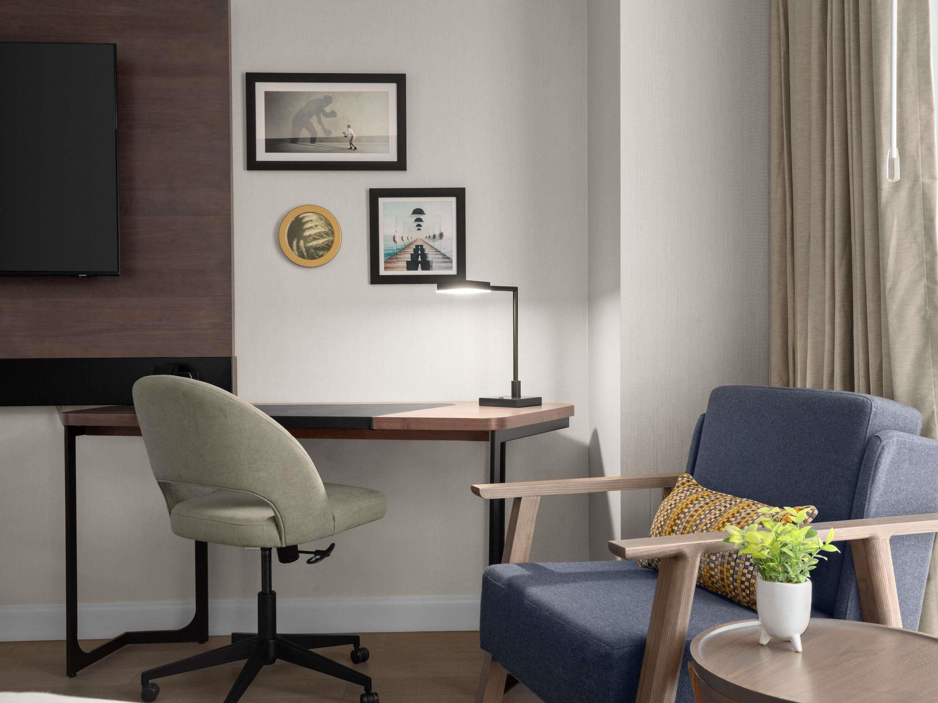 A modern office space with a desk, two chairs, a TV, and framed artwork on the wall.
