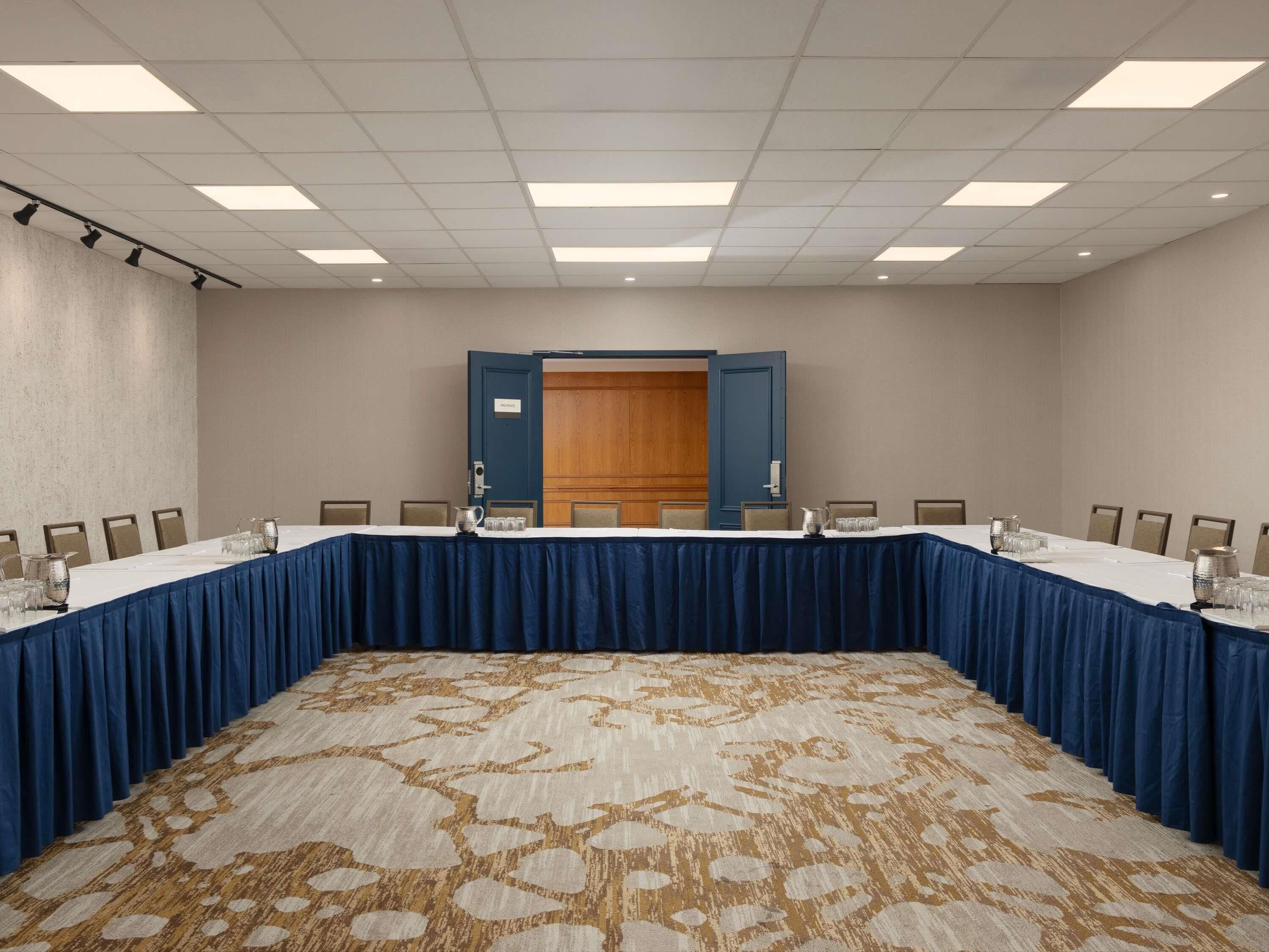 A conference room with a long table, chairs, a carpeted floor, and a wooden door.