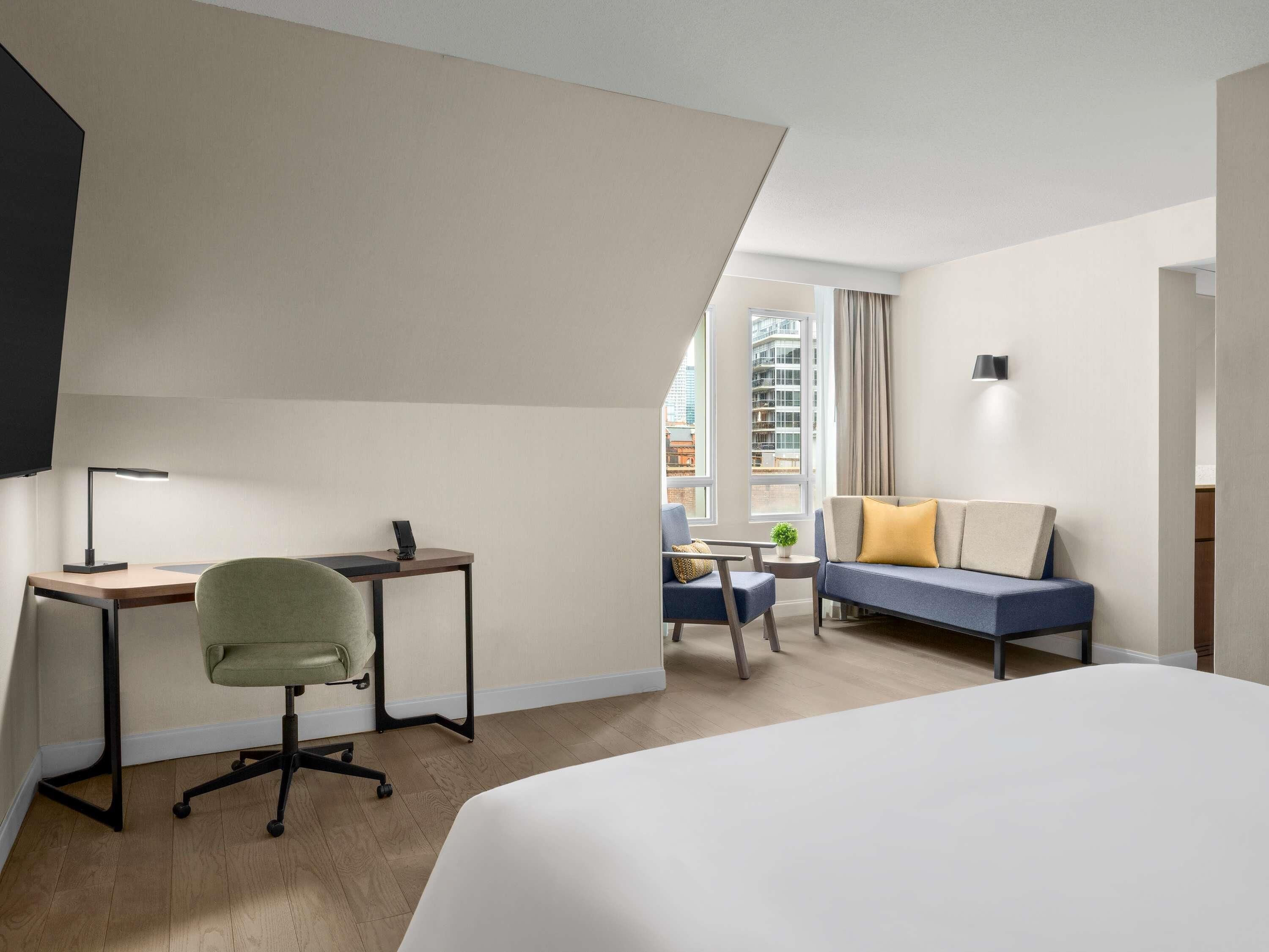 Quarto de hotel com cama, escrivaninha, cadeira e sofá.