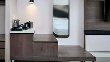 Una habitación de hotel moderna con un escritorio de madera, una cafetera, un espejo y un televisor.