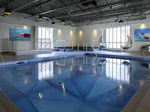 Una piscina interior con agua cristalina, un trampolín y dos amplias ventanas que dejan entrar luz natural.