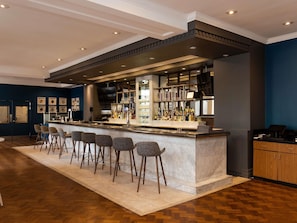 Una zona de bar con mostrador de mármol, taburetes y una selección de botellas.
