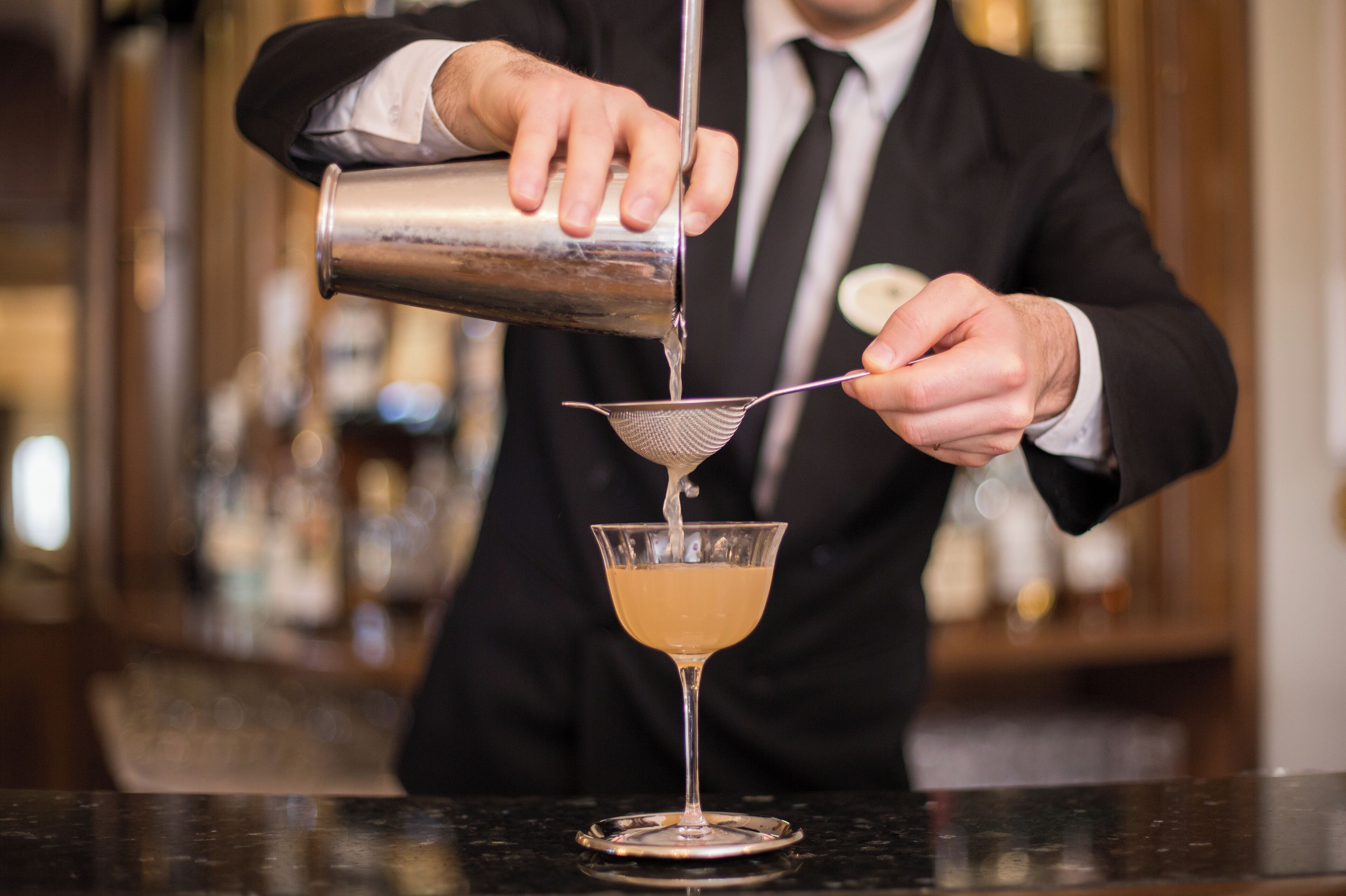 A bartender pouring a drink into a martini glass using a strainer.