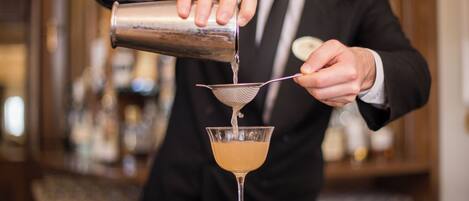 A bartender pouring a drink into a martini glass using a strainer.