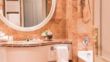A bathroom with a marble sink, a round mirror, a handheld showerhead, and a towel rack.