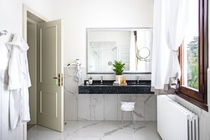 Un baño moderno con suelo de mármol, lavabo doble, secador de pelo, planta en maceta y radiador.