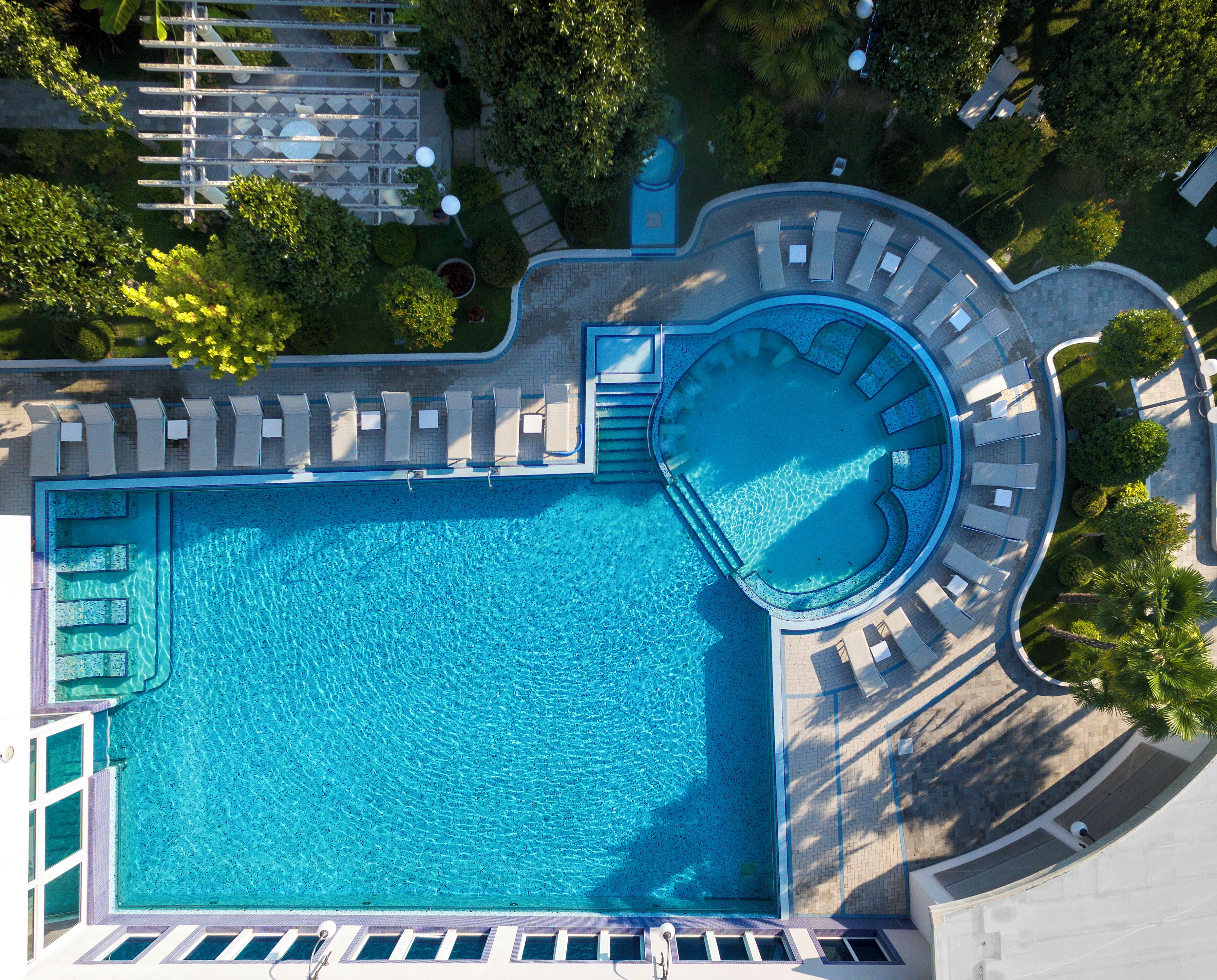 Vista aérea de un hotel con una piscina rectangular grande, tumbonas y una zona de hidromasaje circular.