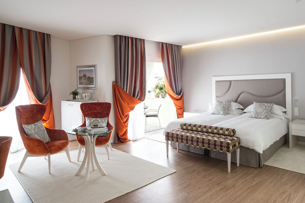 Une chambre d’hôtel moderne avec un grand lit, une table en verre, deux fauteuils et un petit bureau.