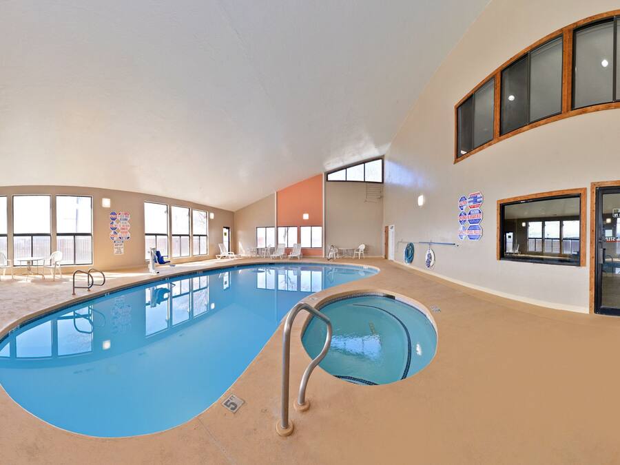 A large indoor swimming pool with multiple lanes, surrounded by lounge chairs and a sunroofed area with large windows.