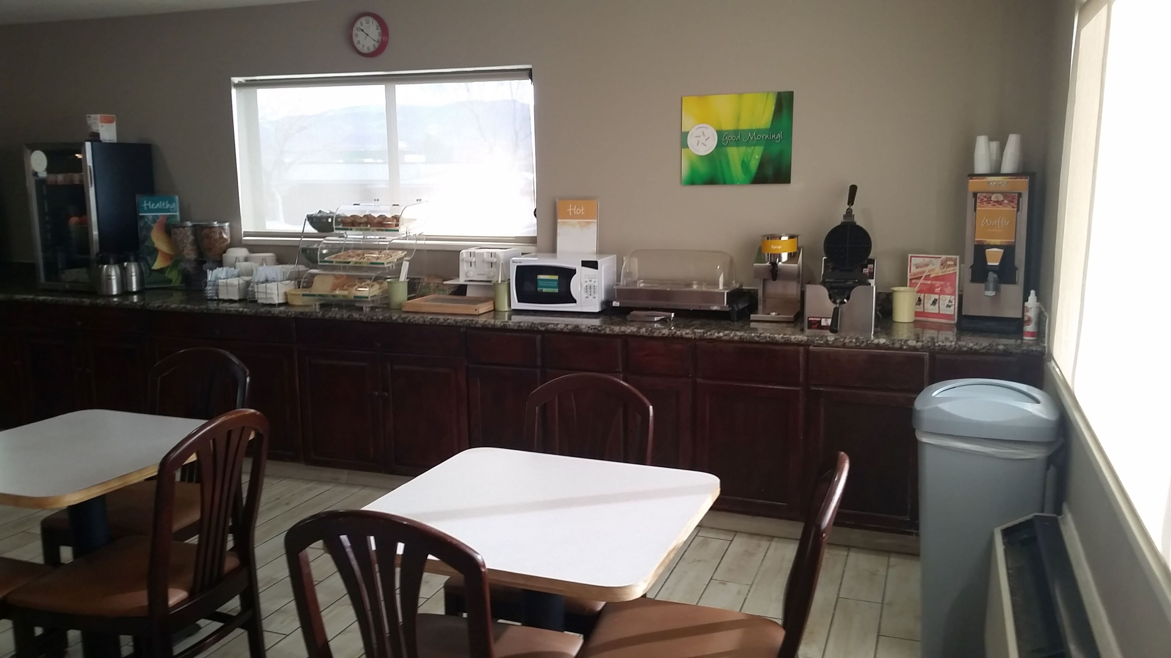A kitchen with a window, a microwave, a coffee machine, and a trash can.