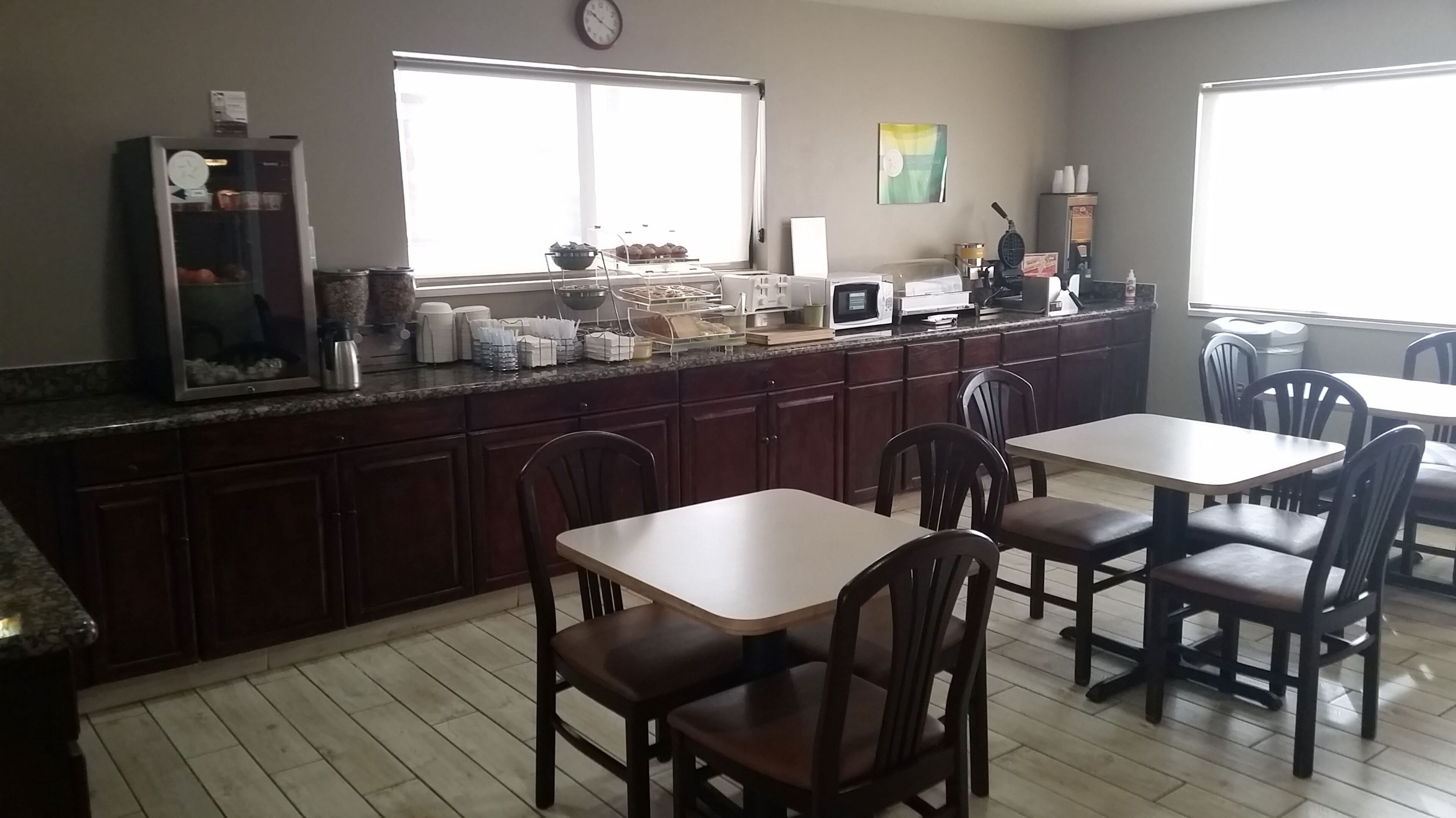 Una cocina con armarios de madera, una encimera con diversos electrodomésticos y una zona de comedor con mesas y sillas.