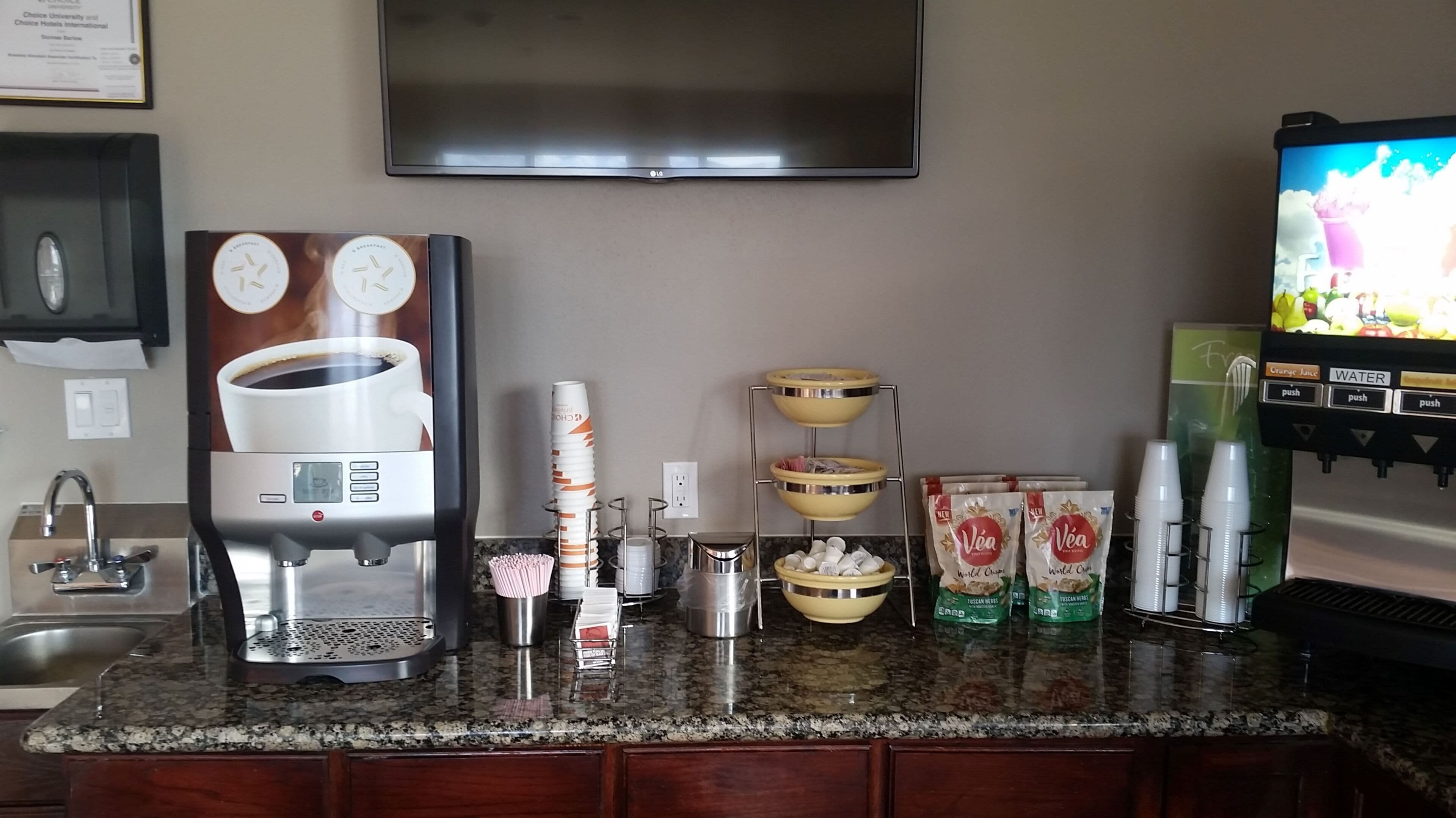 A hotel bar area with a coffee machine, a TV, and beverage dispensers.