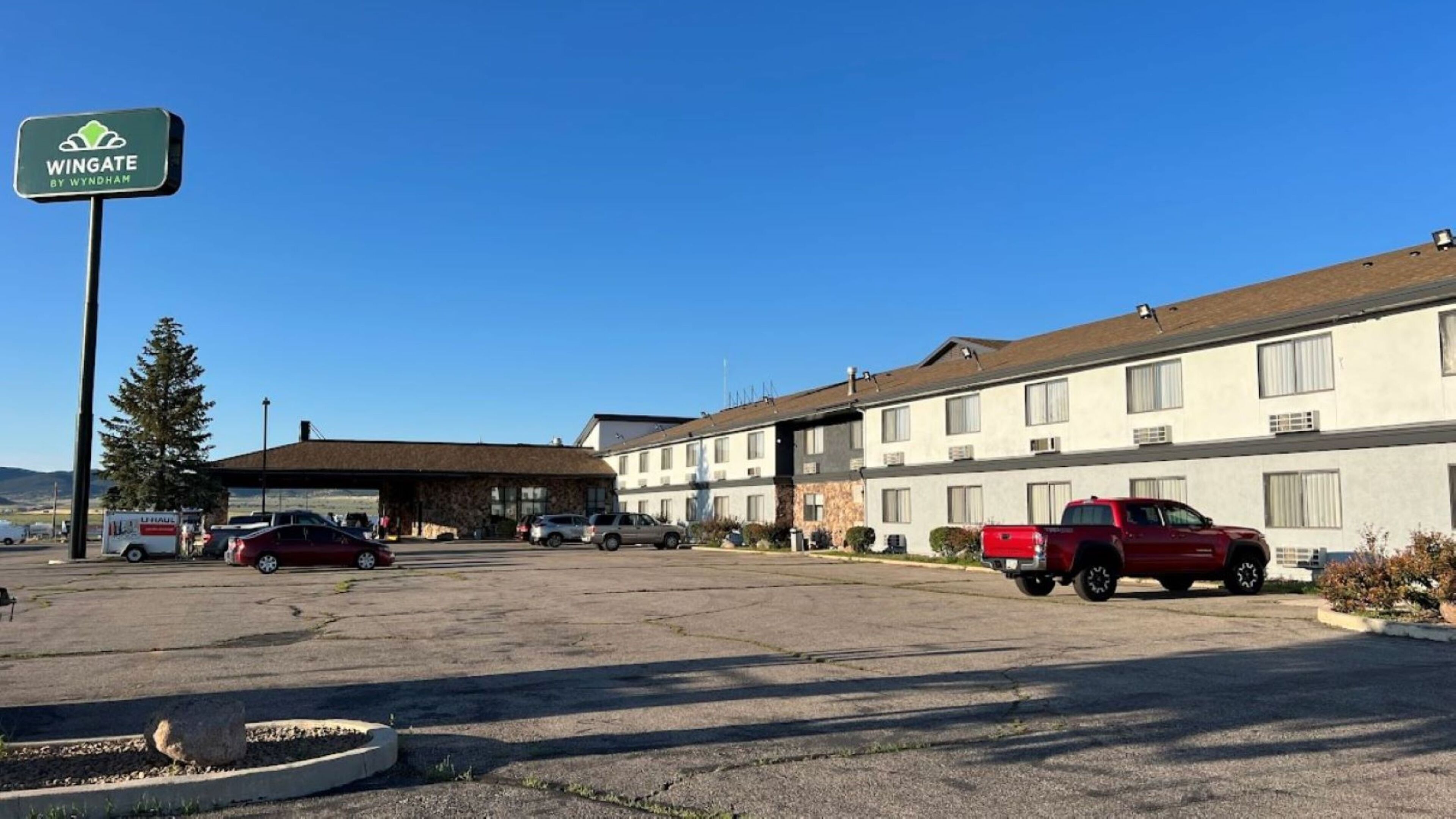 A Wingate by Wyndham motel with a parking lot, a U-Haul truck, and a red pickup truck parked in front.