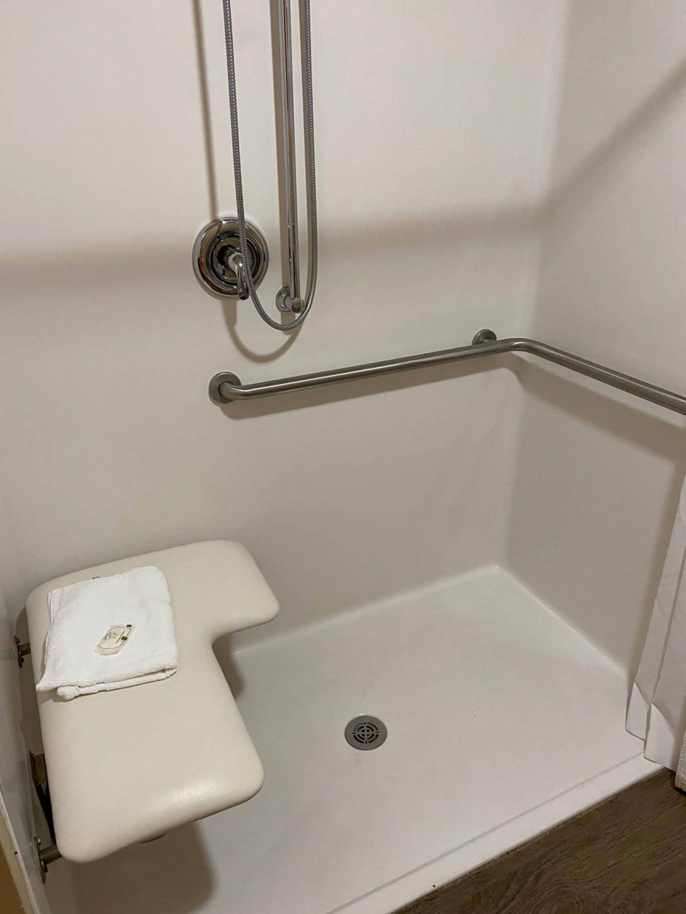 Un box de ducha blanco con una barra de apoyo, un inodoro blanco y un cabezal de ducha.