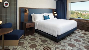 A hotel room with a large bed, a desk, a chair, and a view of the city.