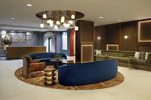 Um lobby moderno com um sofá azul, uma mesa de centro redonda e um balcão de recepção.