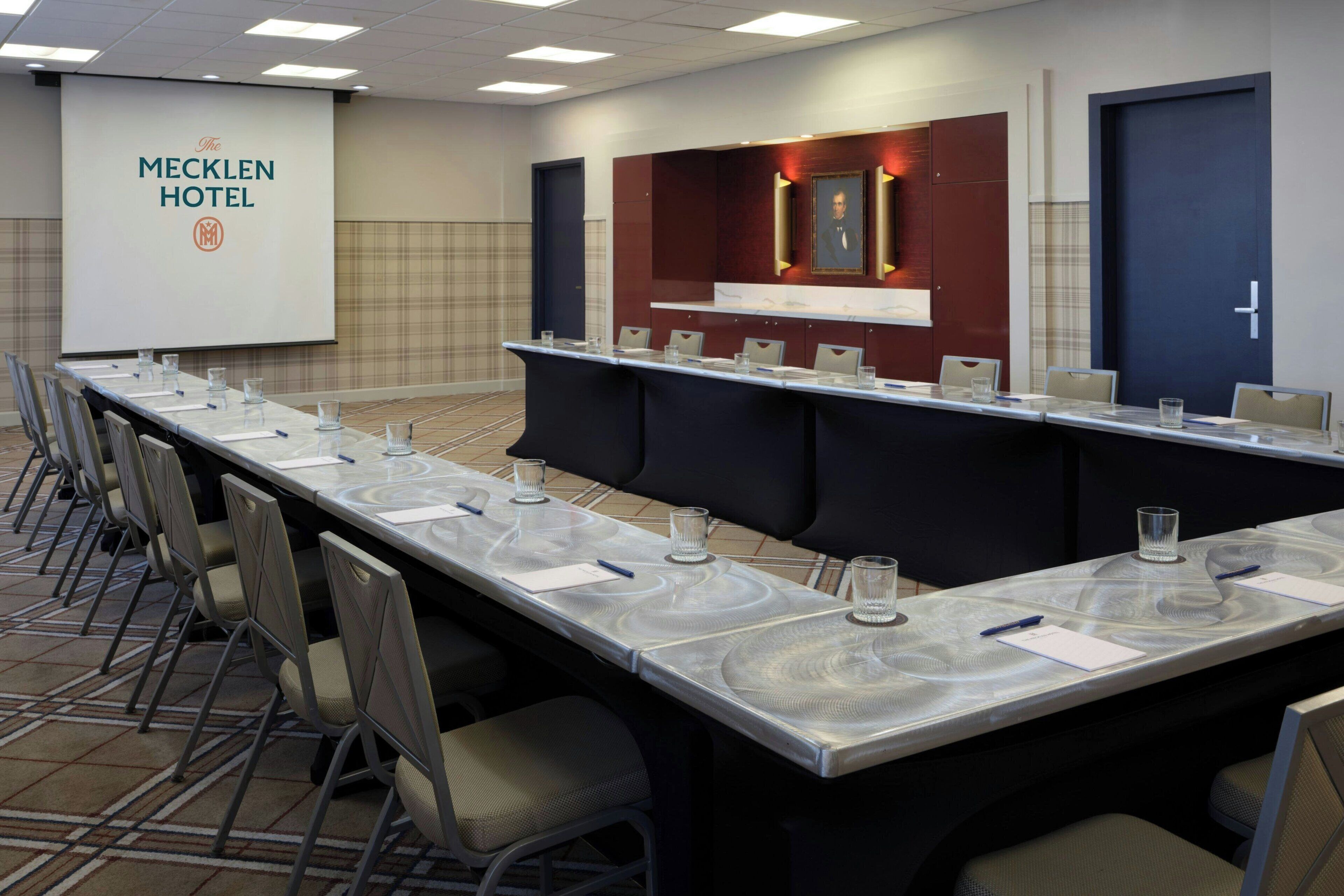 A conference room at The Mecklen Hotel with a long table, chairs, and a projector screen.