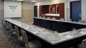 A conference room at The Mecklen Hotel with a long table, chairs, and a projector screen.