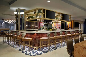 Zona de bar con mostrador de ladrillo, varios taburetes y una gran variedad de botellas.