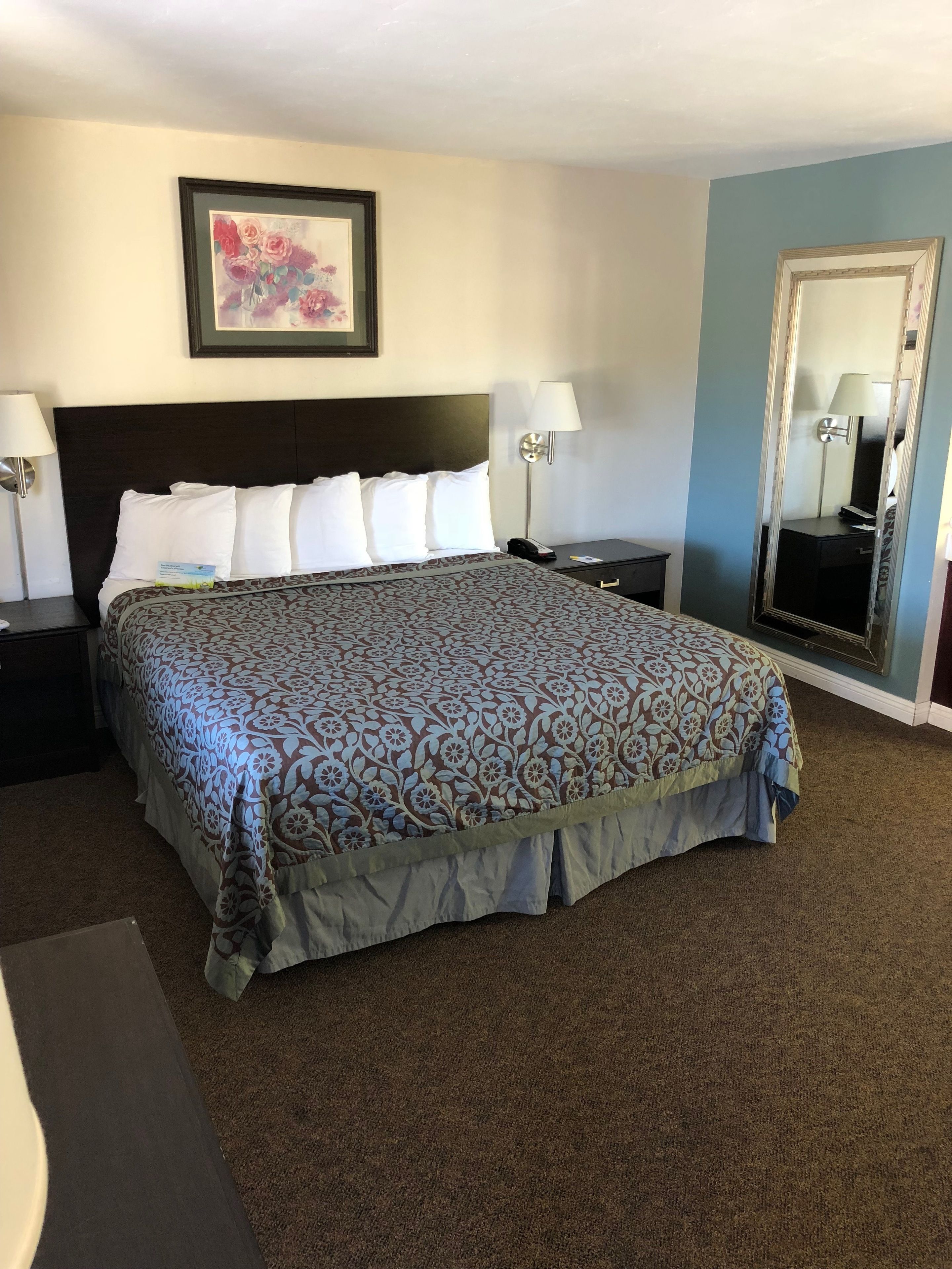 A neatly made bed with a patterned bedspread, two bedside tables with lamps, a framed picture on the wall, and a large mirror.