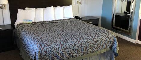 A neatly made bed with a patterned bedspread, two bedside tables with lamps, a framed picture on the wall, and a large mirror.
