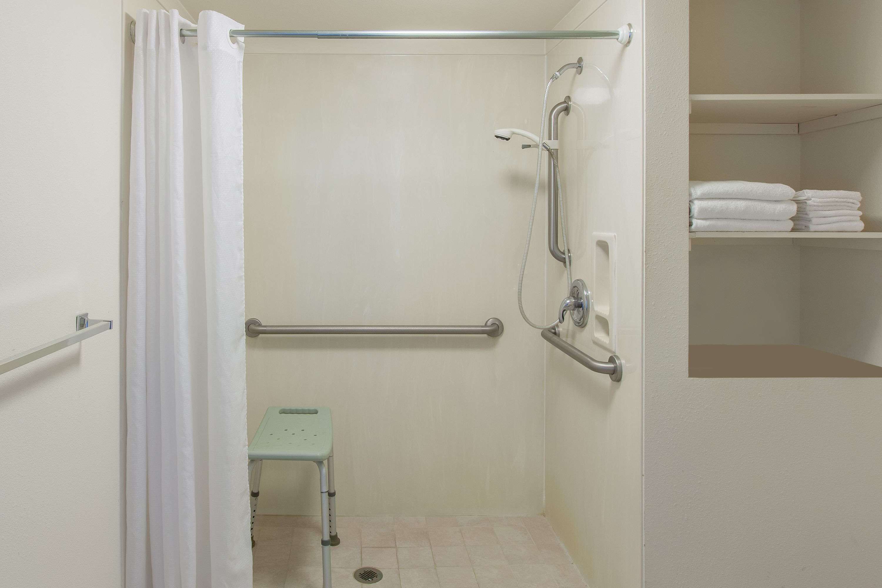 A walk-in shower with a grab bar, a small step stool, and a towel rack.