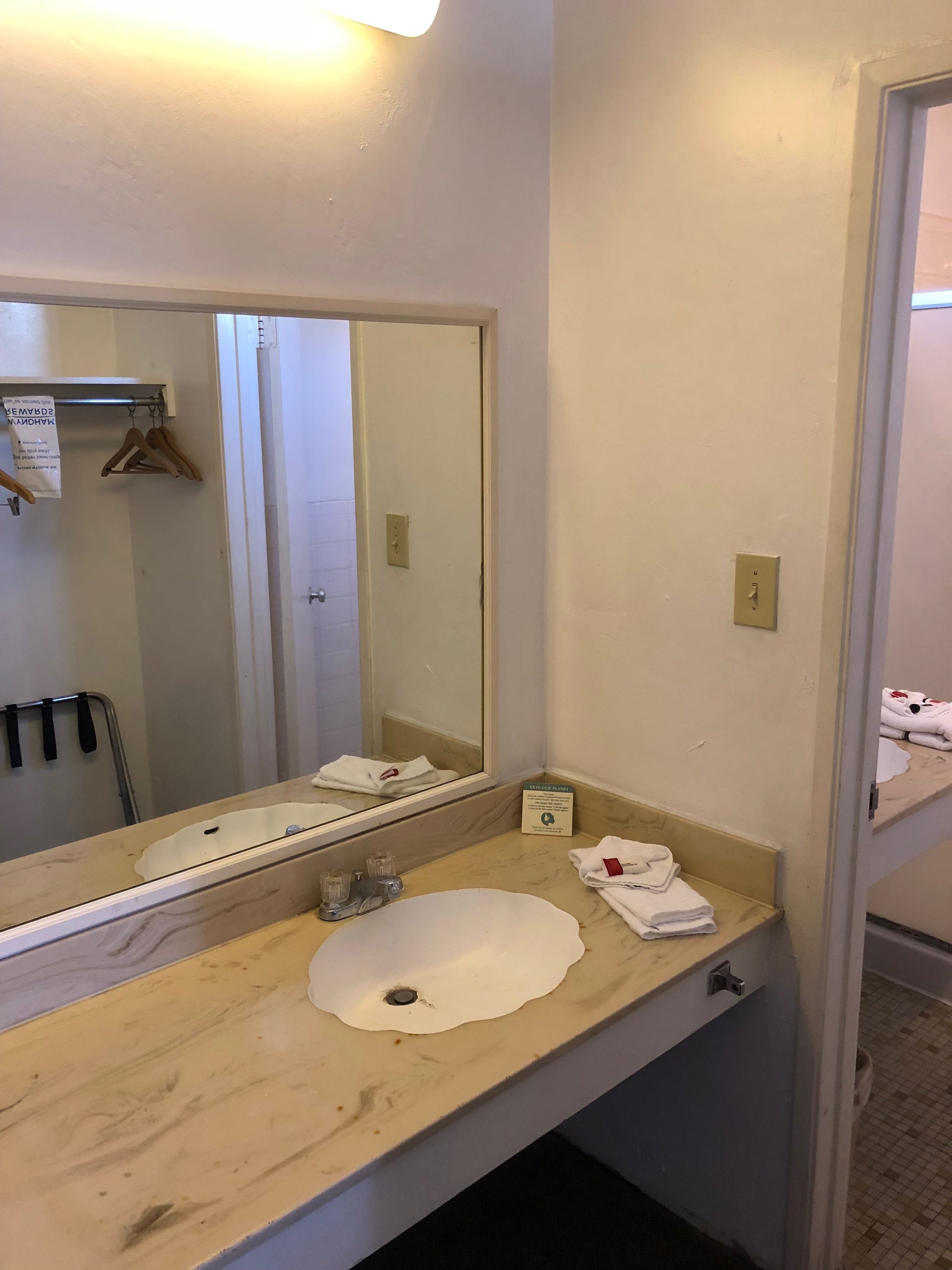 Un baño con lavamanos, espejo, toallero y un cartel en la pared.