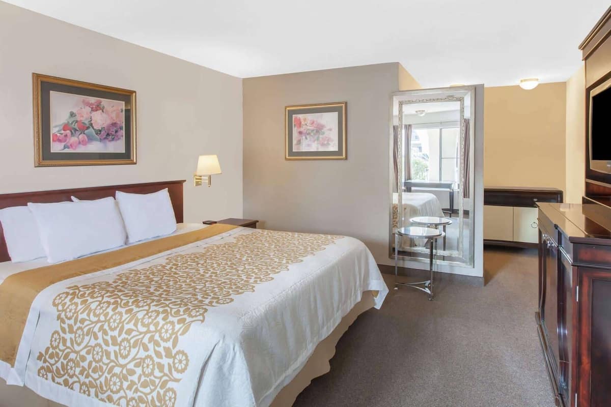 Een hotelkamer met een groot bed, een bureau, een stoel, een televisie en twee wanddecoraties met bloemen.