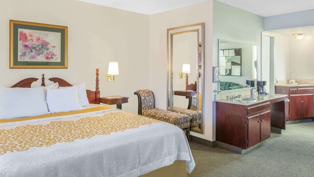 Una habitación de hotel con una cama grande, una silla, un tocador con espejo y una mesita.