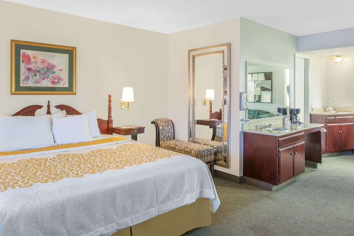 Een hotelkamer met een groot bed, een stoel, een kaptafel met spiegel en een klein tafeltje.