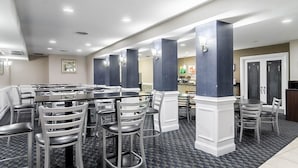 A restaurant with high tables and chairs, a patterned floor, and a view of the kitchen in the background. - Rodeway Inn & Suites Williamsburg Central (Williamsburg)