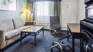 A hotel room with a sofa, a desk, a chair, a television, and a window with curtains. - Rodeway Inn & Suites Williamsburg Central (Williamsburg)