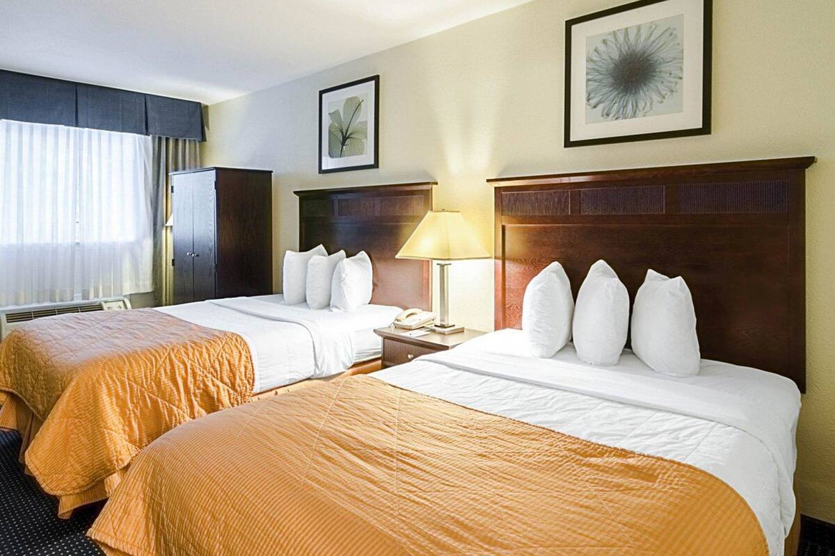 A hotel room with two beds, a nightstand with a lamp, a wardrobe, and a framed picture on the wall.