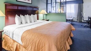 A hotel room with a large bed, a desk, a chair, and a window with curtains. - Rodeway Inn & Suites Williamsburg Central (Williamsburg)