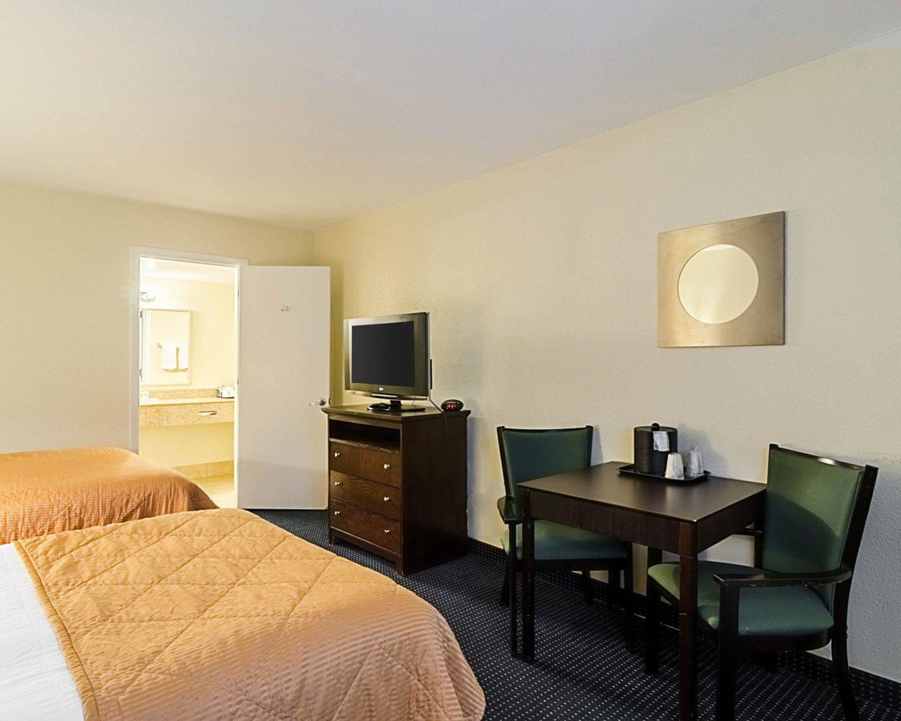 A hotel room with two beds, a TV on a dresser, a table with chairs, and a wall-mounted light.