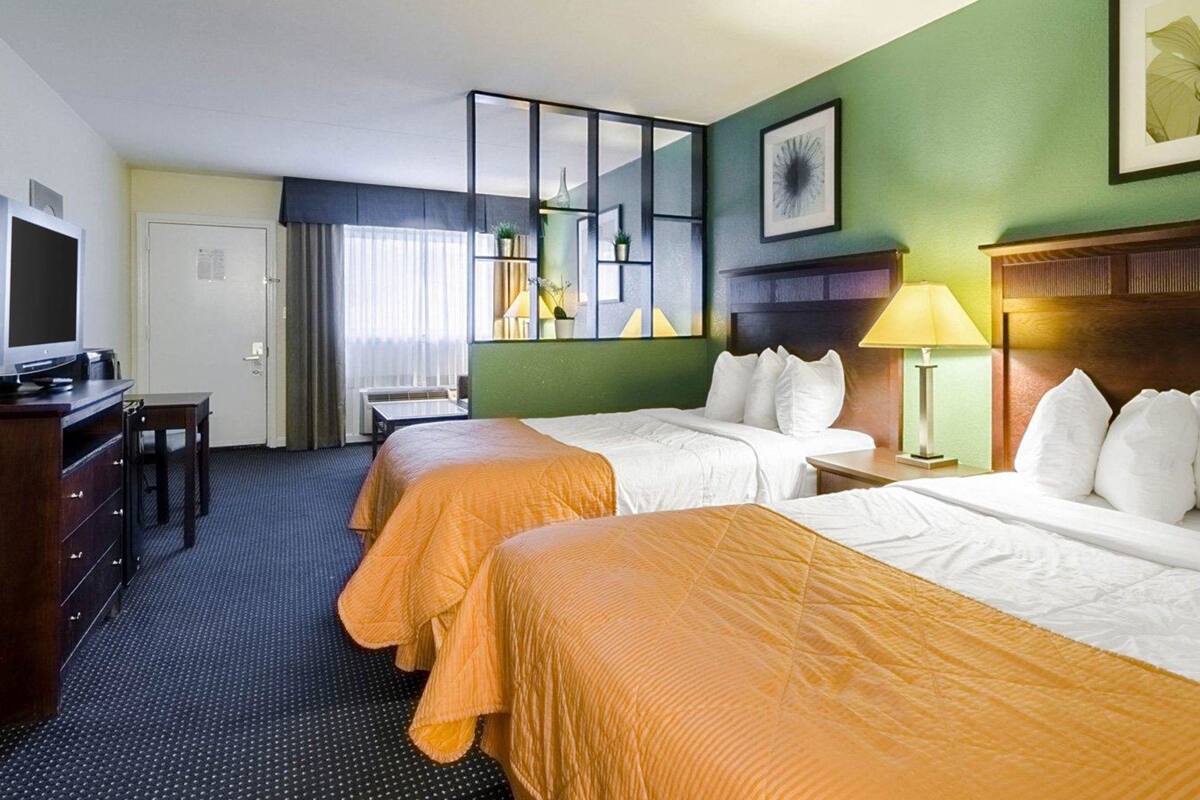 A hotel room with two beds, a desk with a television, a chair, and a window with curtains.