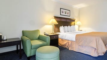 A hotel room with a bed, a green armchair, a small ottoman, a nightstand, and two bedside lamps.